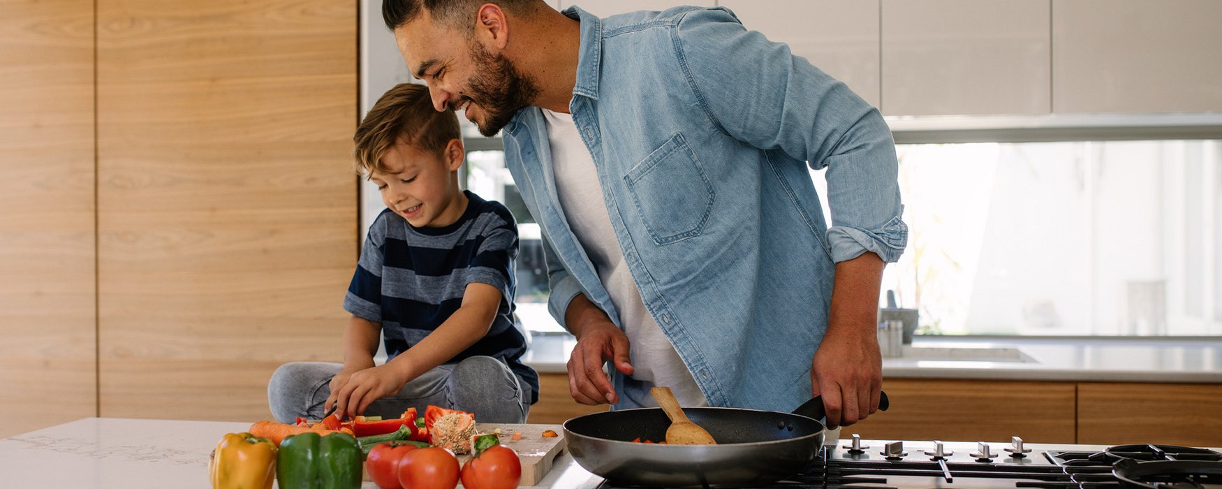 Kleiner Junge schneidet Gemüse, das sein Vater in einer Bratpfanne kochen möchte